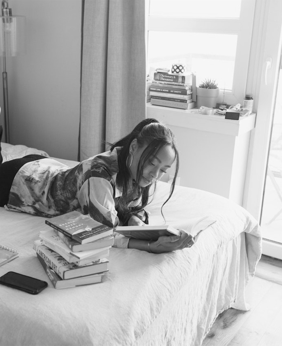 Student studying on her bed surrounded by books
